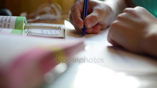 A criança faz seu dever de casa, escreve em um livro de recortes na mesa closeup — Vídeo de Stock