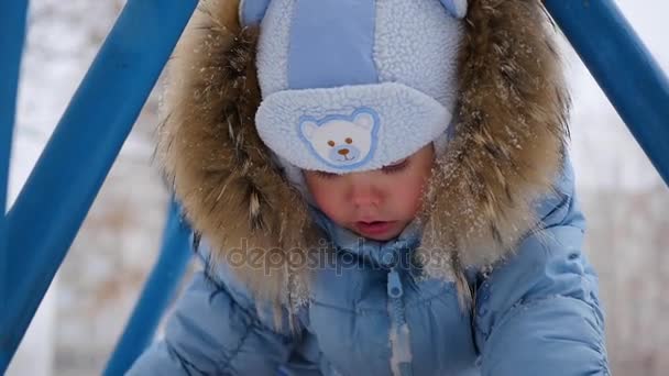 Un pequeño niño feliz juega en el patio de recreo en invierno — Vídeos de Stock
