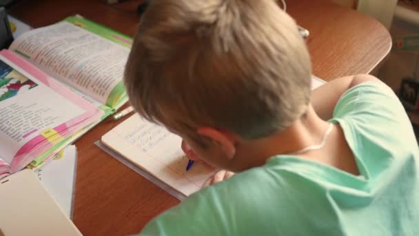 El niño hace su tarea, escribe en un copybook en la mesa — Vídeo de stock