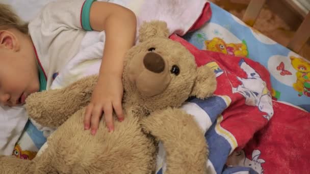 The sweet baby sleeps in a cot with a teddy bear — Stock Video