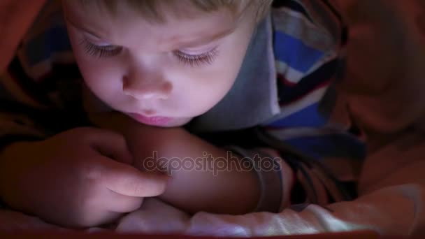 Ein kleiner Junge sieht spätabends Zeichentrickfilme in der Tablette — Stockvideo