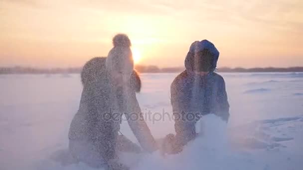 Meisje en kind gooien van sneeuw over zichzelf en geniet in winter park bij zonsondergang — Stockvideo