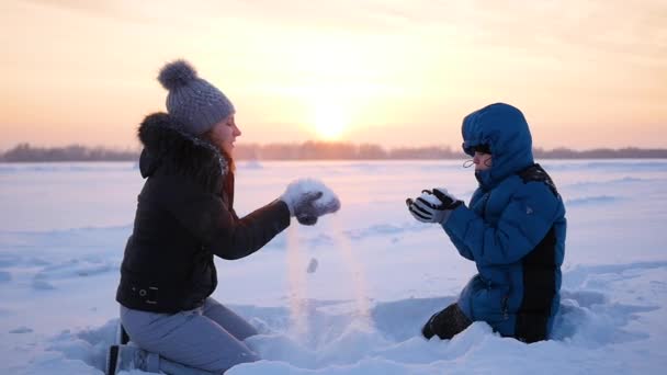 Girl and child throwing snow over himself and enjoys it in winter park at sunset — Stock Video