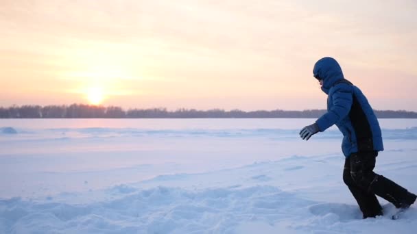 Tiener speelt op de speelplaats in de winter. Deze methode spiegelt in de sneeuw bij zonsondergang — Stockvideo