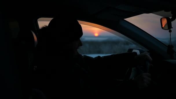 O tipo vai atrás do volante de um carro. silhueta no tempo de inverno no pôr do sol — Vídeo de Stock