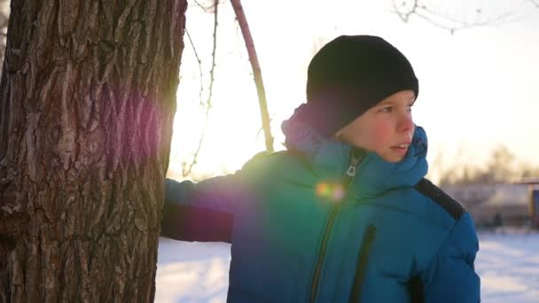 Niño feliz se para cerca de un árbol y sonríe en el soleado día de invierno — Vídeos de Stock