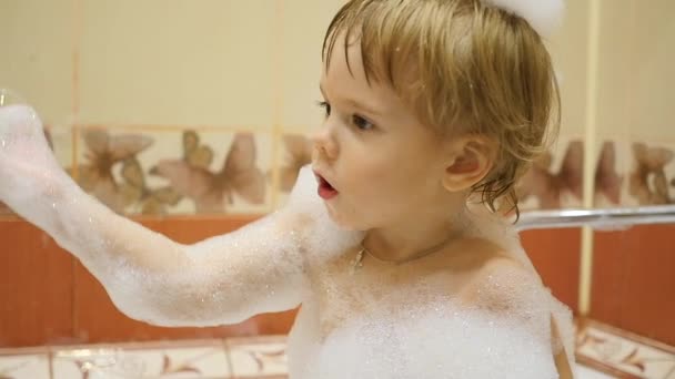 Ребенок веселится, играя с пеной и мыльными пузырями в ванной — стоковое видео