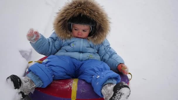 Mutlu bir çocuk snowtube içinde karlı bir tepe üzerinde sürmek. — Stok video