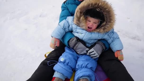 Un niño feliz cabalga y cae en tubo de nieve en una colina nevada — Vídeos de Stock