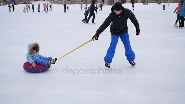 Молодой человек на катке катает ребенка на снегоходе — стоковое видео