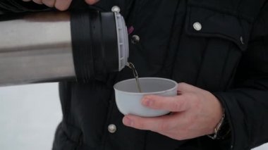 adam açık havada bir termos sıcak çay dökülen. Kış saati