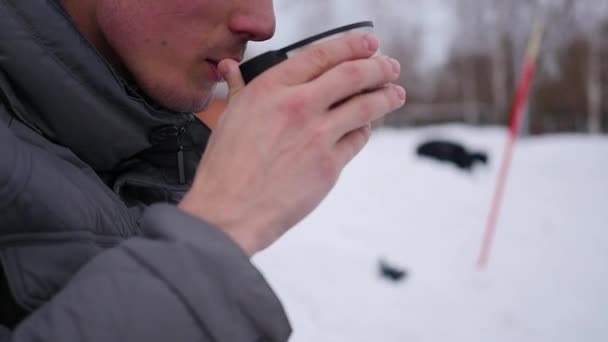 El tipo está bebiendo té caliente de una taza en el invierno al aire libre. pista de hielo . — Vídeos de Stock