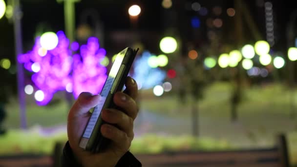 Ο άνθρωπος γραπτών μηνυμάτων sms χρησιμοποιώντας app στο smartphone τη νύχτα στην πόλη, Χειμερινή ώρα. κινηματογράφηση σε πρώτο πλάνο — Αρχείο Βίντεο