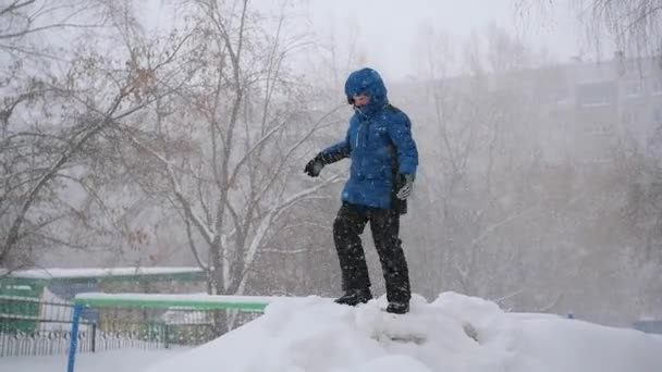 Dziecko skacze na śniegu w winter park. Burza śnieżna — Wideo stockowe