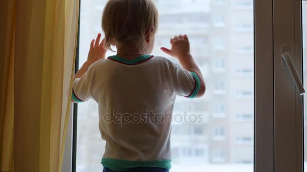 Ein Kind steht auf der Fensterbank und schaut aus dem Fenster — Stockvideo