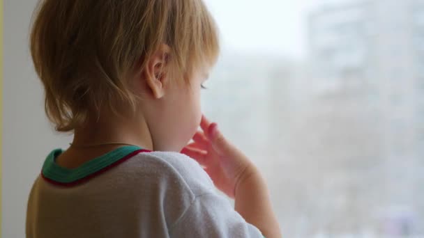 Un niño se para en el alféizar de la ventana y mira por la ventana de cerca — Vídeo de stock