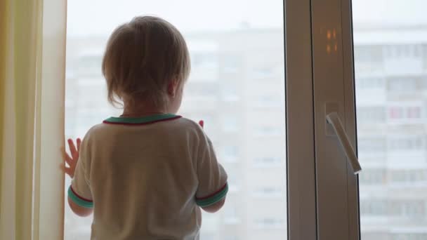 Ребенок стоит на подоконнике и смотрит в окно — стоковое видео