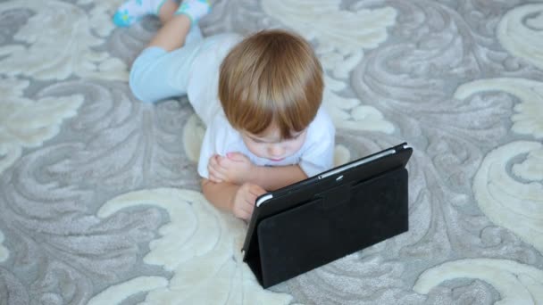 Το παιδί φαίνεται κινούμενα σχέδια σε tablet pc στο πάτωμα — Αρχείο Βίντεο