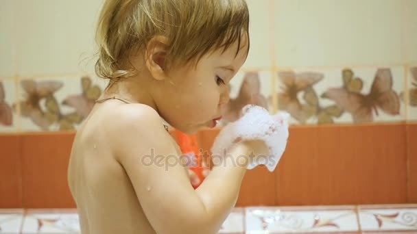 Niño se divierte jugando con espuma en el baño. Soplos de espuma con palmas — Vídeo de stock