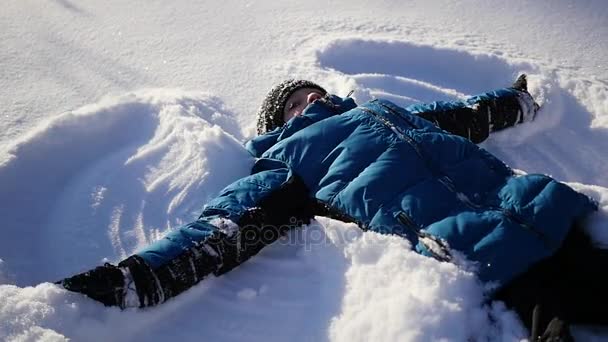 Il bambino giace sulla neve e fa un angelo della neve al rallentatore — Video Stock