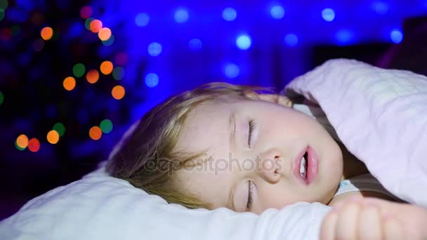 Bellissimo bambino che dorme sul letto la notte di Natale. Sullo sfondo luci e ghirlande di abete — Video Stock