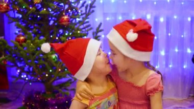 İki kız kardeş kucaklamak ve öpmek Noel partisinde. Arka plan, ışıklar ve Noel köknar çelenk