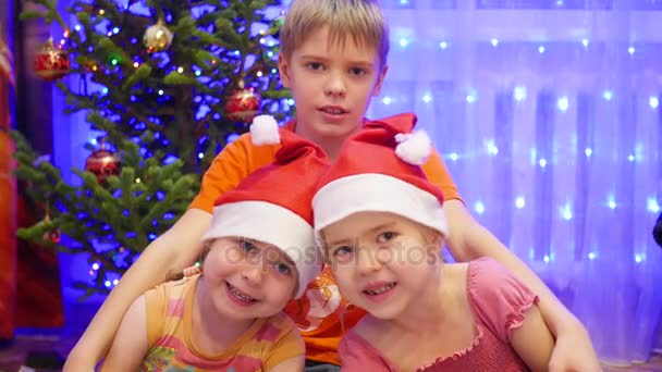 Τα παιδιά που αγκαλιάζει και χαμογελώντας στο Χριστουγεννιάτικο πάρτι. Στο παρασκήνιο, φώτα και γιρλάντες από έλατα Χριστουγέννων — Αρχείο Βίντεο
