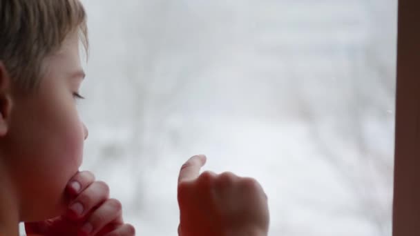 Teenager zeigt mit dem Finger auf die Fensterscheibe. Schnee draußen in Unschärfe — Stockvideo