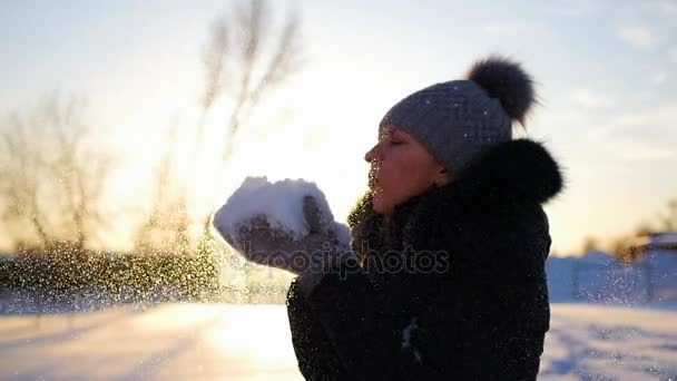 Ragazza soffia neve con le mani su sfondo tramonto — Video Stock