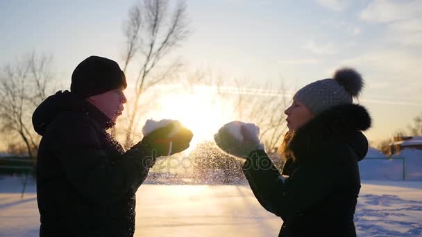 Dziewczyna i facet śniegu ciosy rękami na tle zachodu słońca — Wideo stockowe