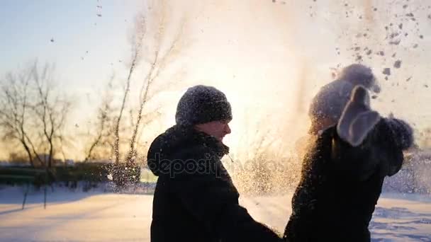 Un ragazzo e una ragazza getta neve sopra la testa e abbraccia sullo sfondo del tramonto — Video Stock