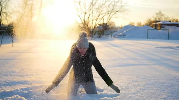 女の子は、夕日を背景に頭の上の雪をスローします。 — ストック動画