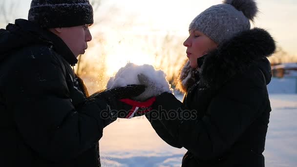 Дівчина і хлопець дме сніг руками на фоні заходу сонця — стокове відео