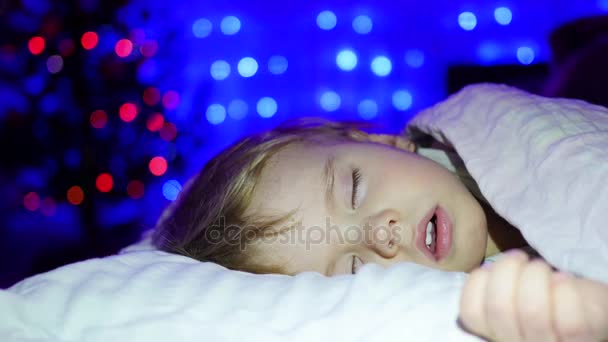 Piękne dziecko śpi na łóżku noc Bożego Narodzenia. W tle, światła i Girlandy choinkowe — Wideo stockowe