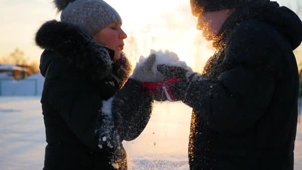 Fille et gars souffle neige avec les mains sur fond de coucher de soleil — Video