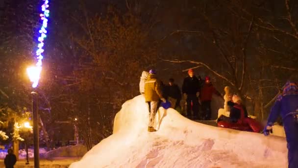 NOVOSIBIRSK, RÚSSIA - 30 de dezembro de 2016: As crianças se divertem no deslizamento de gelo descendo a colina à noite — Vídeo de Stock