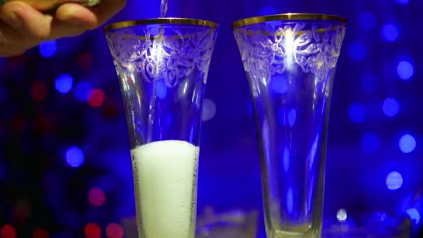 Vinho espumante é derramado em copos. No fundo, bokeh luzes e guirlandas de abeto de Natal — Vídeo de Stock