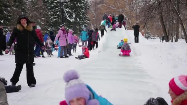 Novosibirsk, Rusland - 31 December 2016:Children veel plezier op de dia ijs naar beneden de heuvel in de dag. — Stockvideo