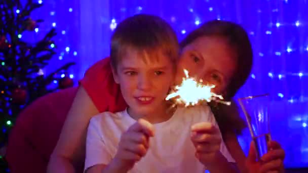 Lycklig familj tända tomtebloss på festen. I bakgrunden, bokeh ljus och kransar av jul fir — Stockvideo