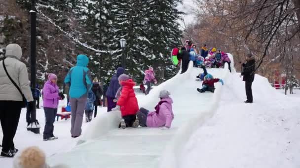 NOVOSIBIRSK, RÚSSIA - 3 de janeiro de 2016: As crianças se divertem no deslizamento de gelo descendo a colina durante o dia . — Vídeo de Stock