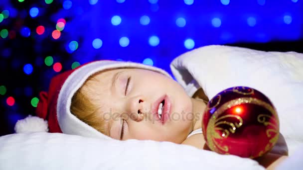 Beautiful baby sleeping on the bed Christmas night. In the background, lights and garlands of fir — Stock Video