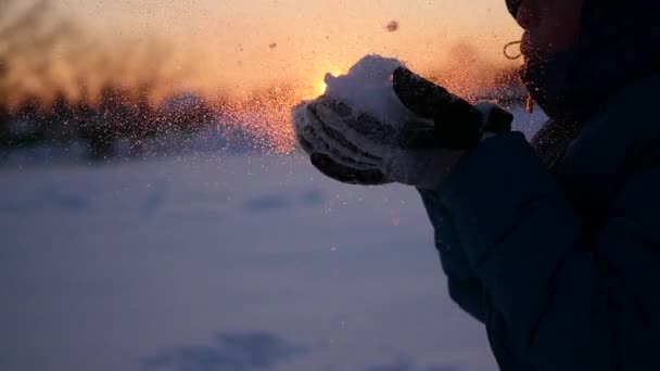 Підліток дме сніг руками на фоні заходу сонця — стокове відео