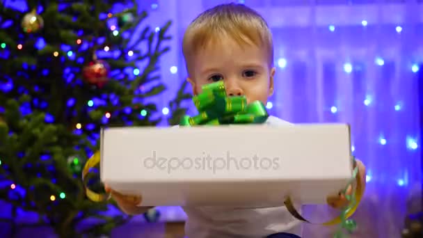 Χριστούγεννα δώρο έκπληξη - ένα παιδί ανοίγει το παρόν. Στο παρασκήνιο, bokeh φώτα και γιρλάντες. — Αρχείο Βίντεο