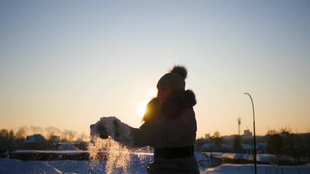 Дівчина кидає сніг над головою на фоні заходу сонця — стокове відео