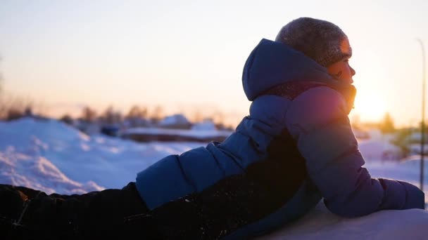 A gyermek feküdt a hó, és néztem a naplementét. téli Park — Stock videók