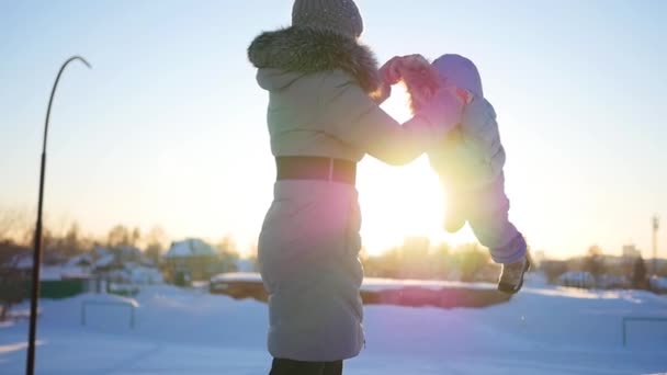 Fille joue avec bébé au coucher du soleil en hiver. Tourner en tenant la main — Video
