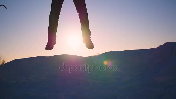 Хлопець стрибає на сніговому схилі і піднімає руки на заході сонця. спорт на відкритому повітрі — стокове відео