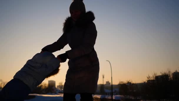 A menina brinca com o bebê ao pôr-do-sol no inverno. Circulando de mãos dadas — Vídeo de Stock