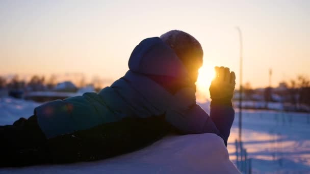 Ett barn vågor handen i winter Park, i bakgrunden av solnedgången. snö vinterlandskap. Solnedgång — Stockvideo
