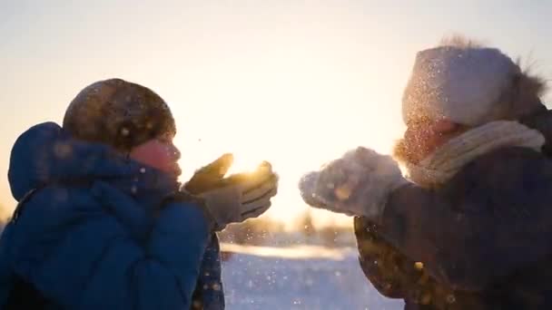 Chica y chico sopla nieve con las manos en el fondo de la puesta del sol. nieve invierno paisaje. Tiempo de puesta del sol — Vídeos de Stock